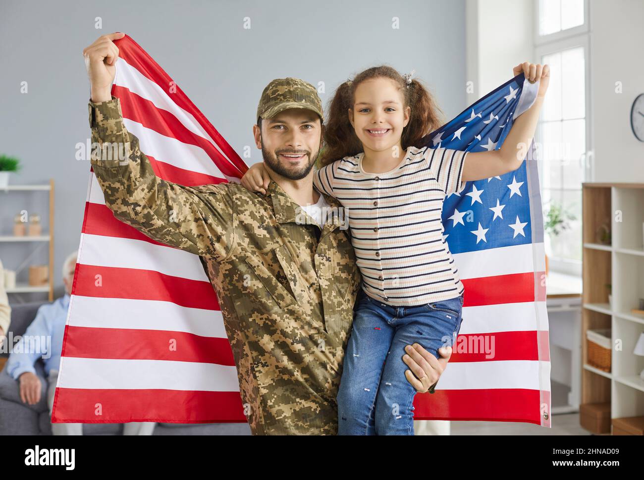 Portrait of a military father and his daughter holding an American flag while standing at home. Stock Photo