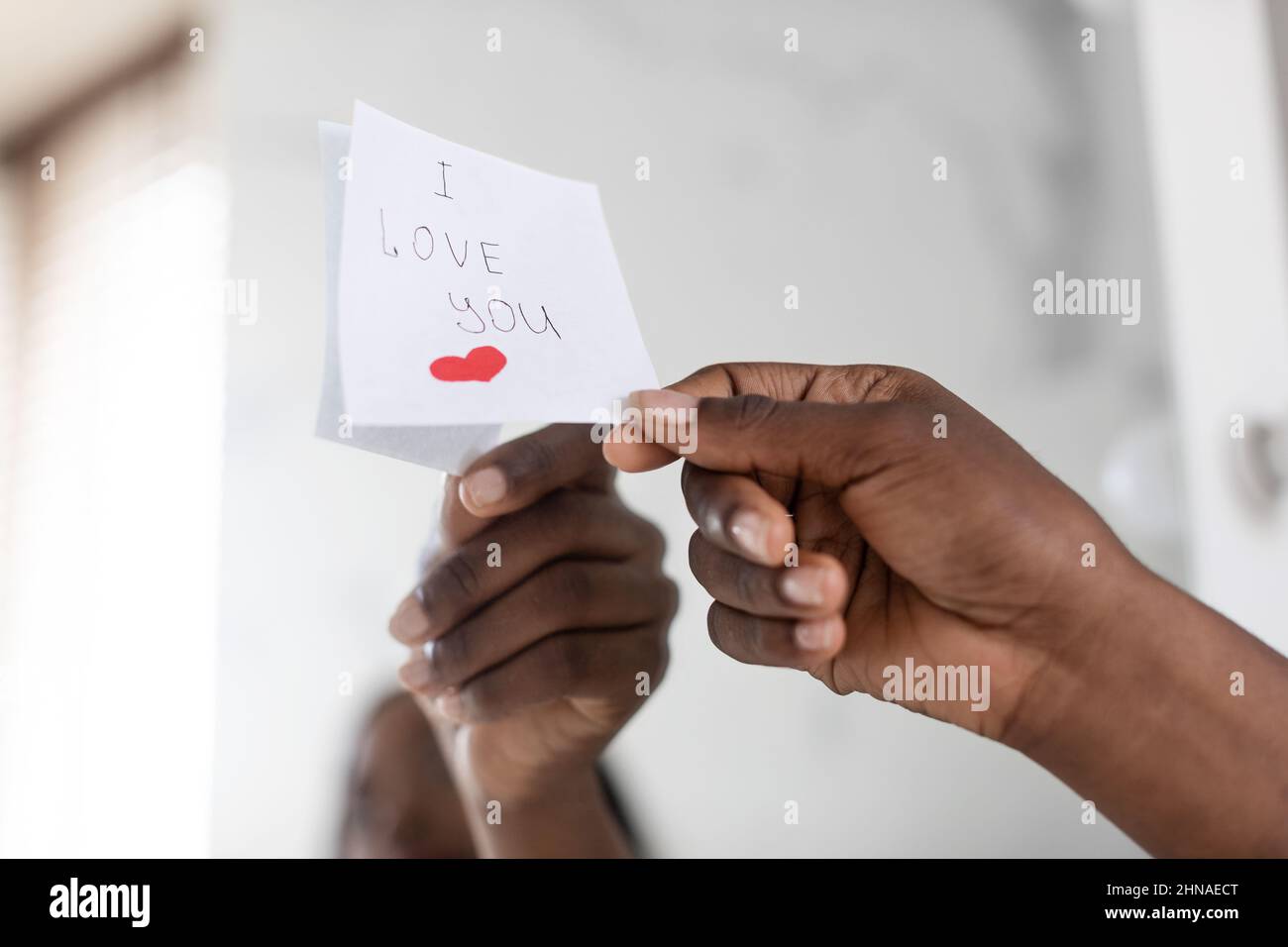 Black Female Hand Putting Sticky Note With Love Message On Mirror, Closeup Stock Photo