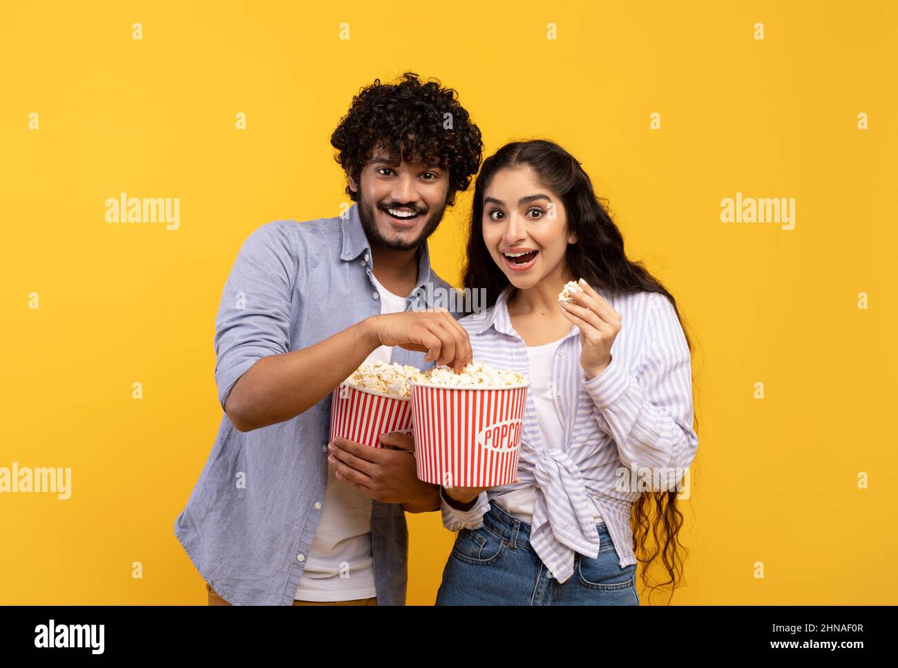 Amazing entertainment, leisure time together. Surprised indian guy and lady eating popcorn and watching movie Stock Photo