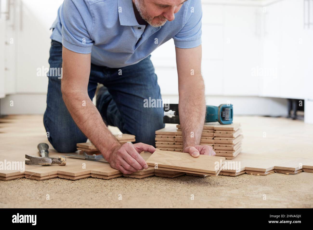 Carpenter Or Builder Laying New Oak Wood Block Parquet Floor In Kitchen At Home Stock Photo