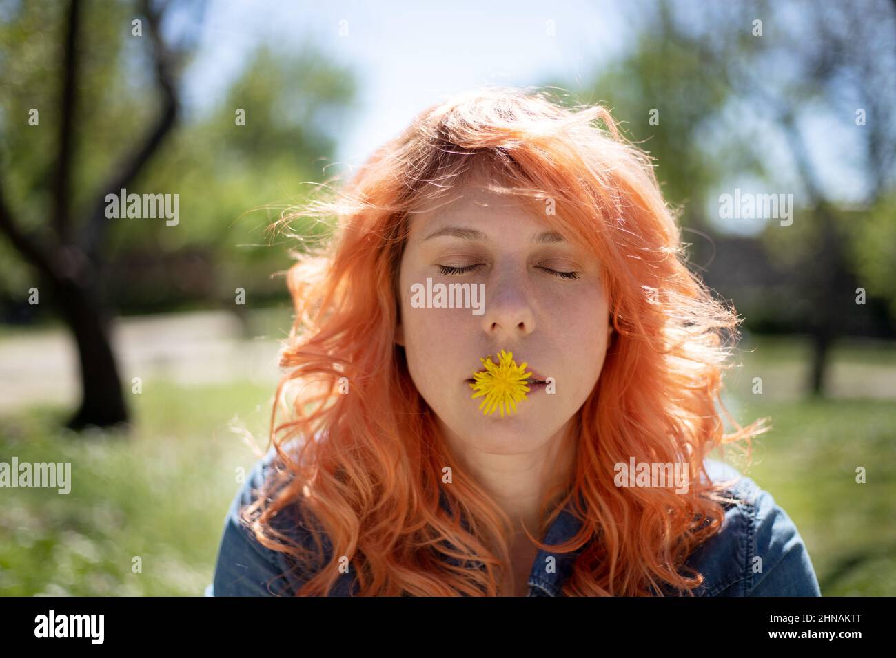 portrait of red-haired woman with flower in her mouth and closed eyes in nature Stock Photo