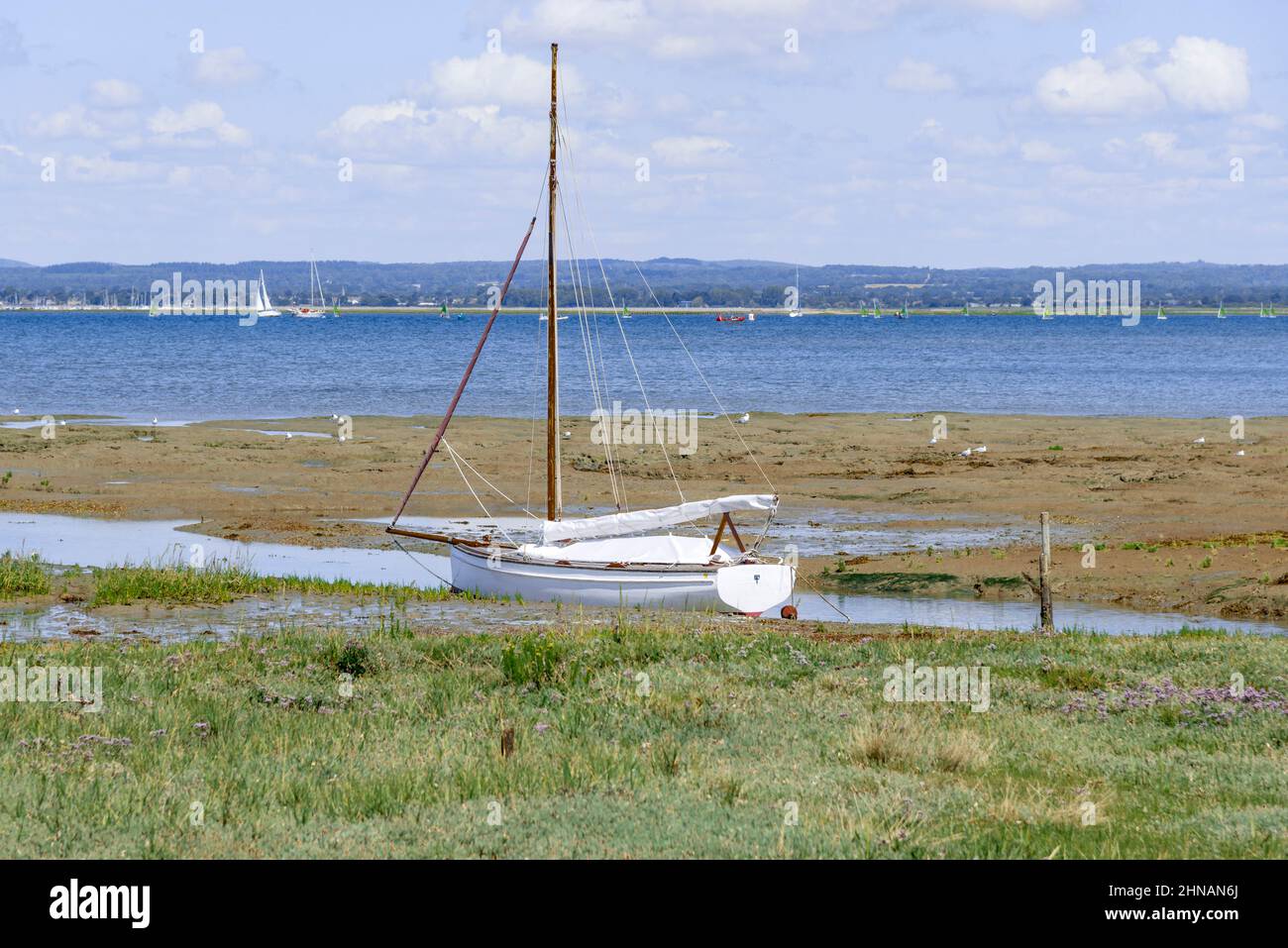 Picturesque scene of boat moored at low tide in Chichester Harbour with Hayling Island in the far distance near Chichester, West Sussex, England, UK Stock Photo
