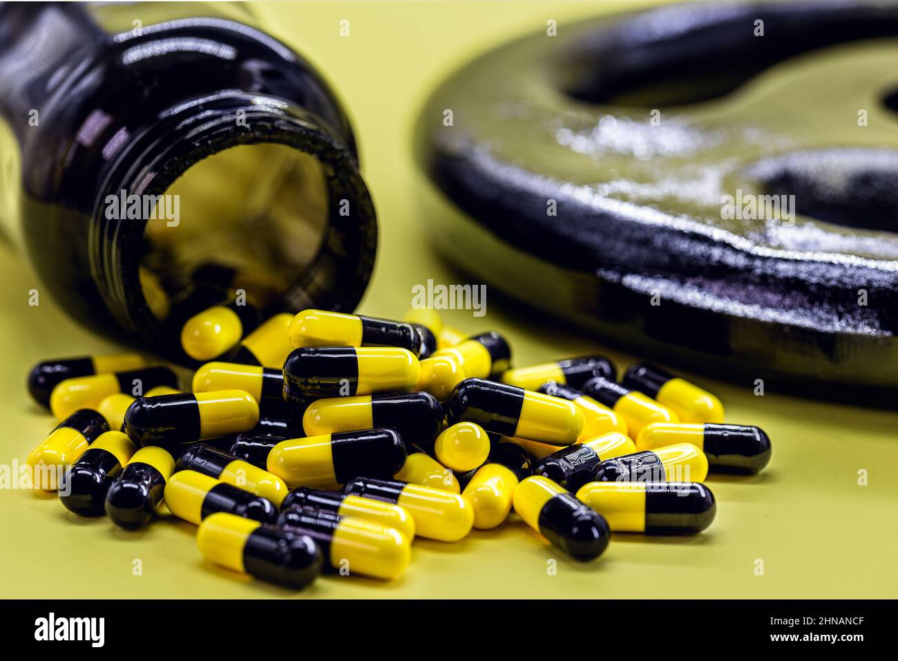 casein or caffeine food supplement capsules for bodybuilding and physical activities, with dumbbells in the background of vibrant yellow color Stock Photo