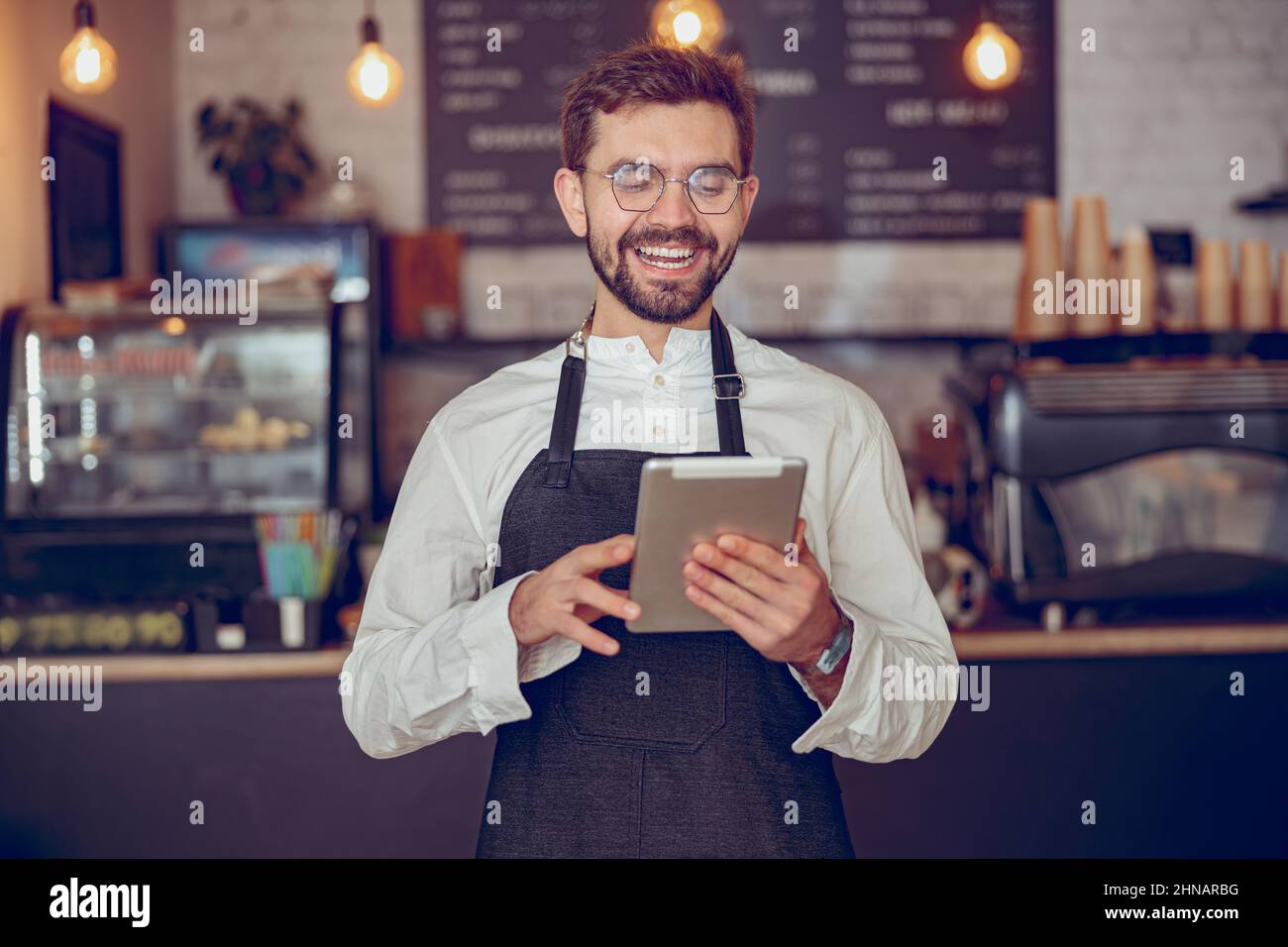 Joyful man barista using tablet computer in cafeteria Stock Photo