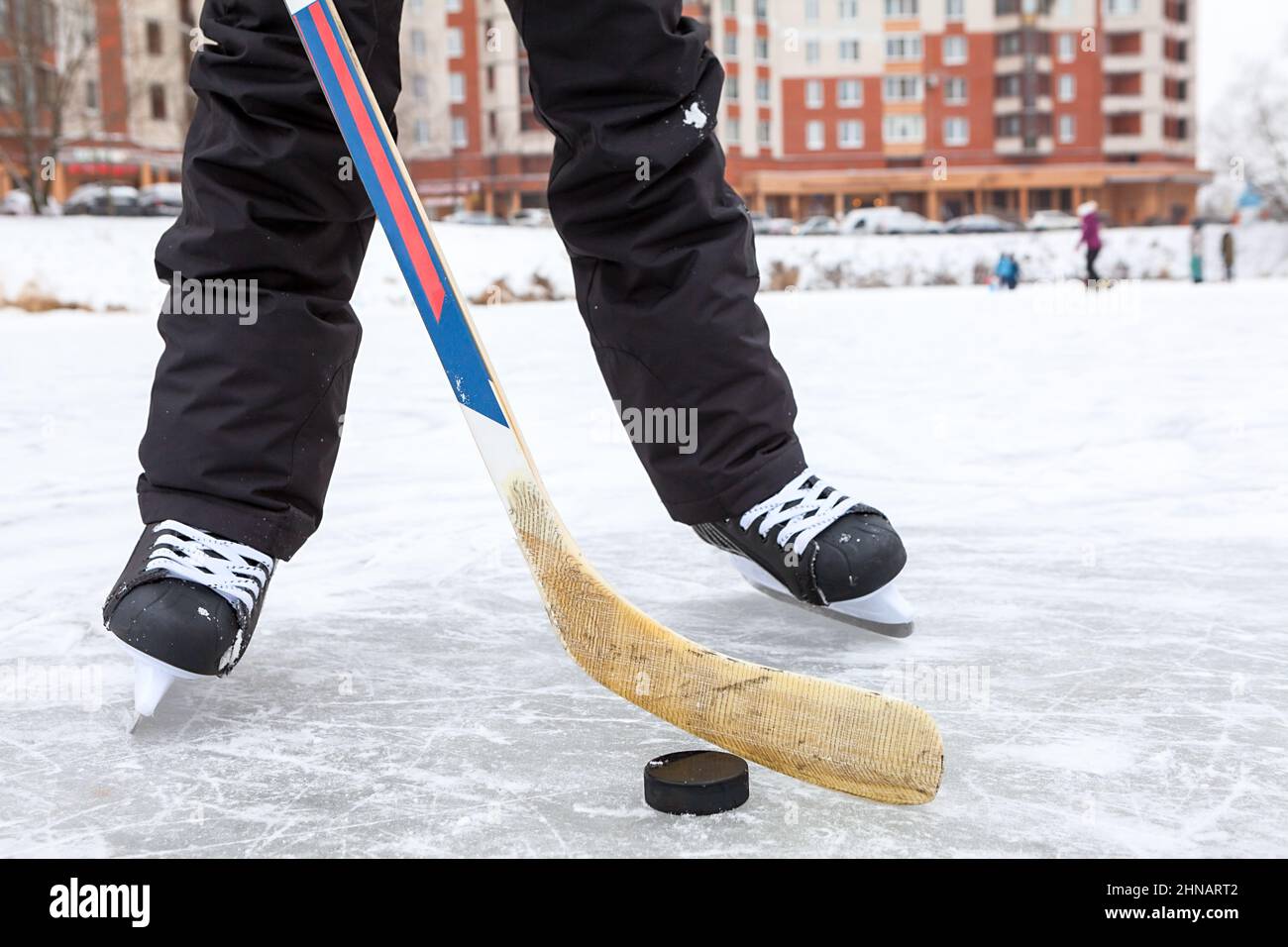 Forward holding black puck with stick, hockey skates on a lake ice, teenage male legs, front view Stock Photo