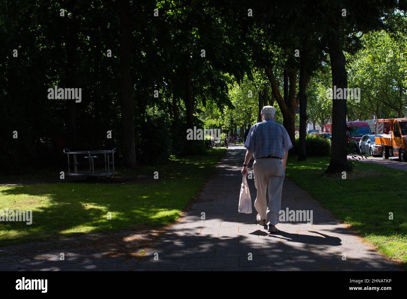 Elderly man walking down a sunlit path between trees in a park Stock Photo