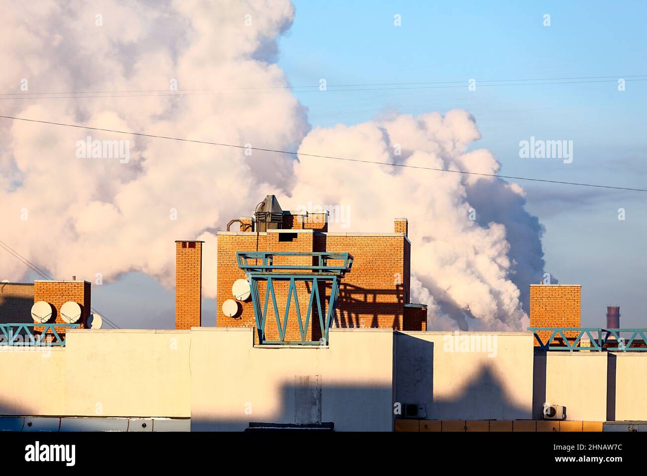A lot of smoke is on background of building roof, sunny weather Stock Photo