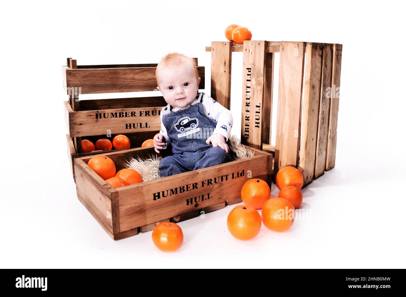 Happy infant boy with red hair playing in an orange fruit box Stock Photo