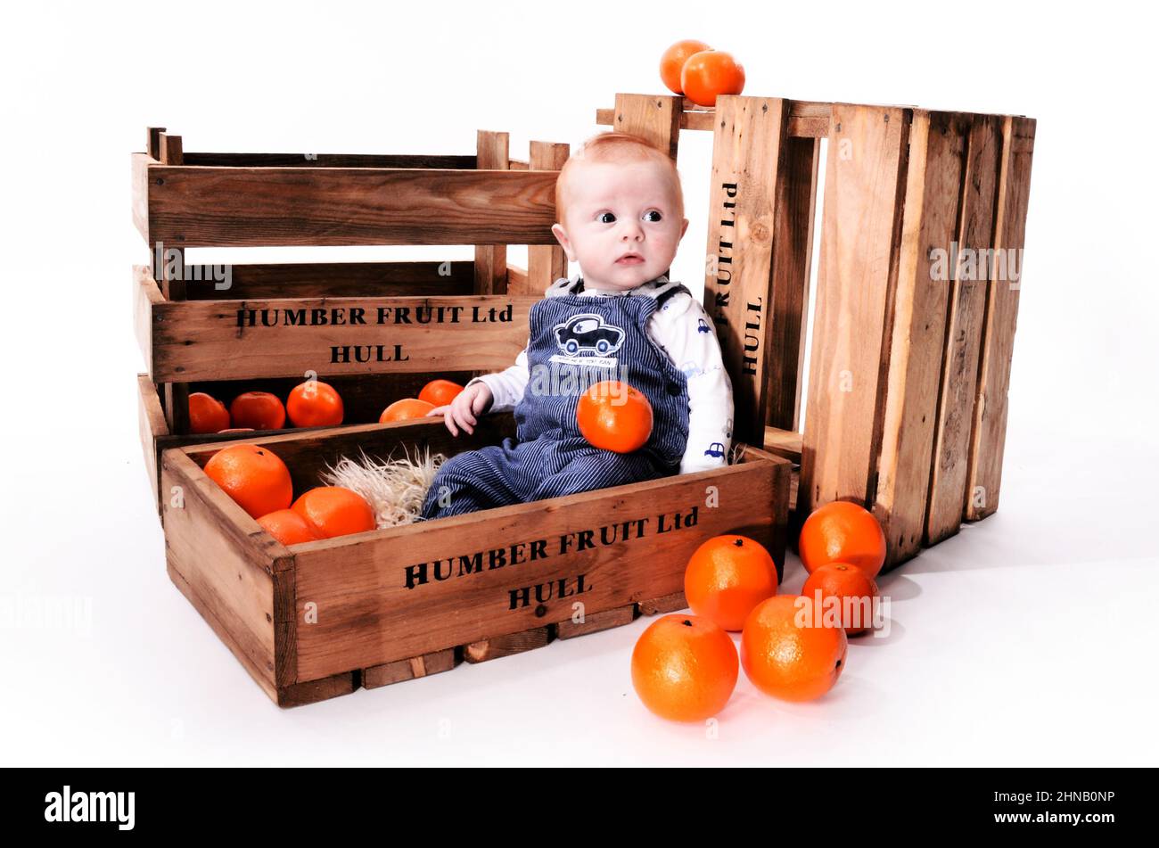 Happy infant boy with red hair playing in an orange fruit box Stock Photo