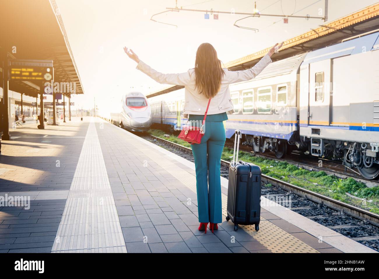 Business woman with trolley bag lost the train because arrived late to the station platform - Beautiful girl waving hands disperated Stock Photo