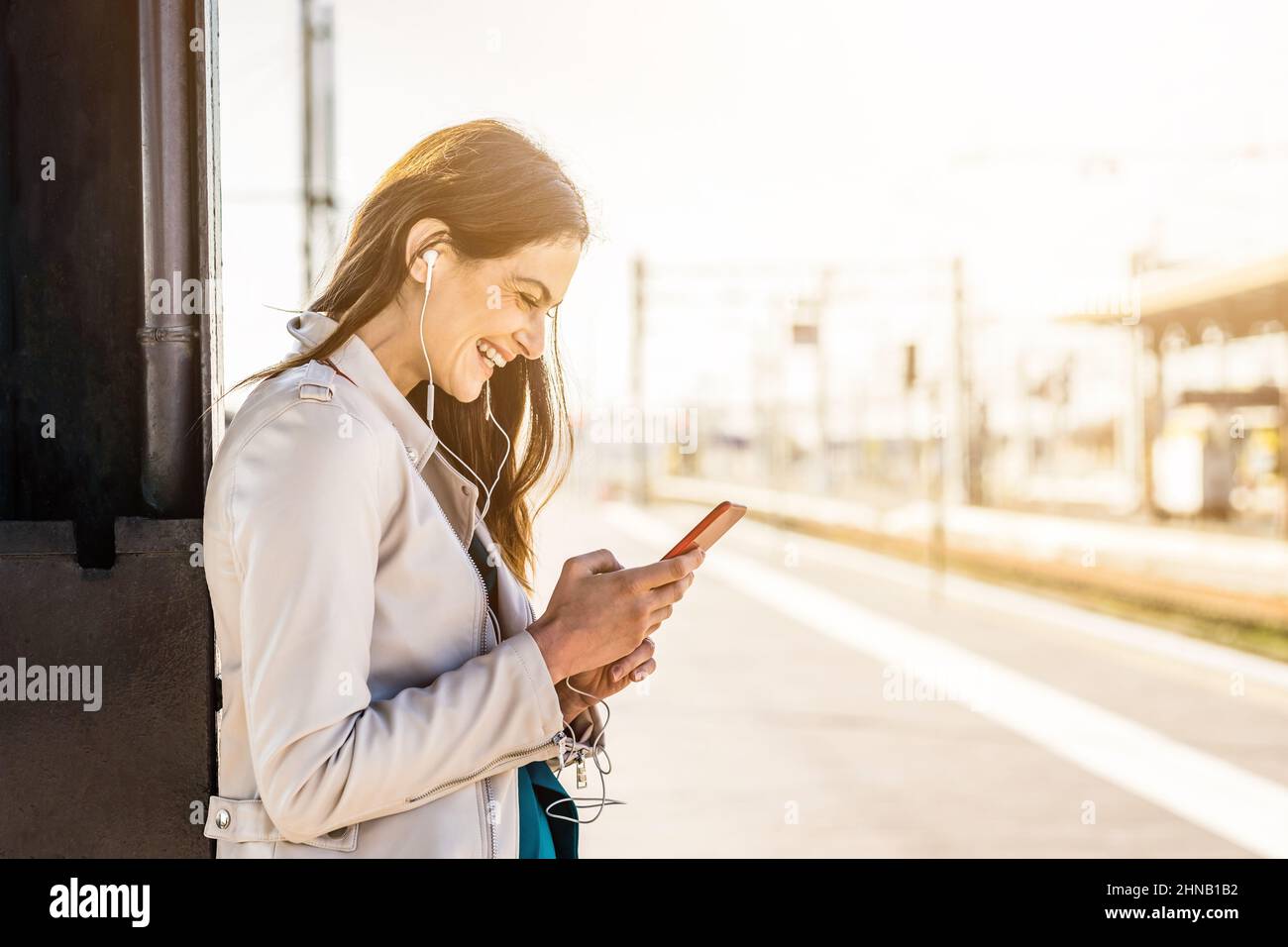 Smiling business woman using smartphone while waiting in a train station - Attractive young student girl using cell-phone while standing Stock Photo