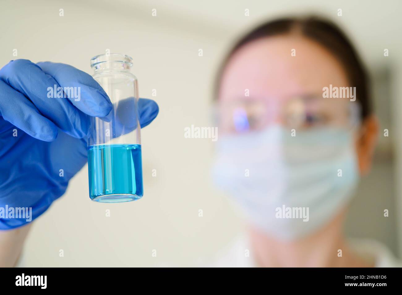 Serious female scientific researcher in gloves looking at a test tube with blue liquid in a laboratory. Close up. Stock Photo