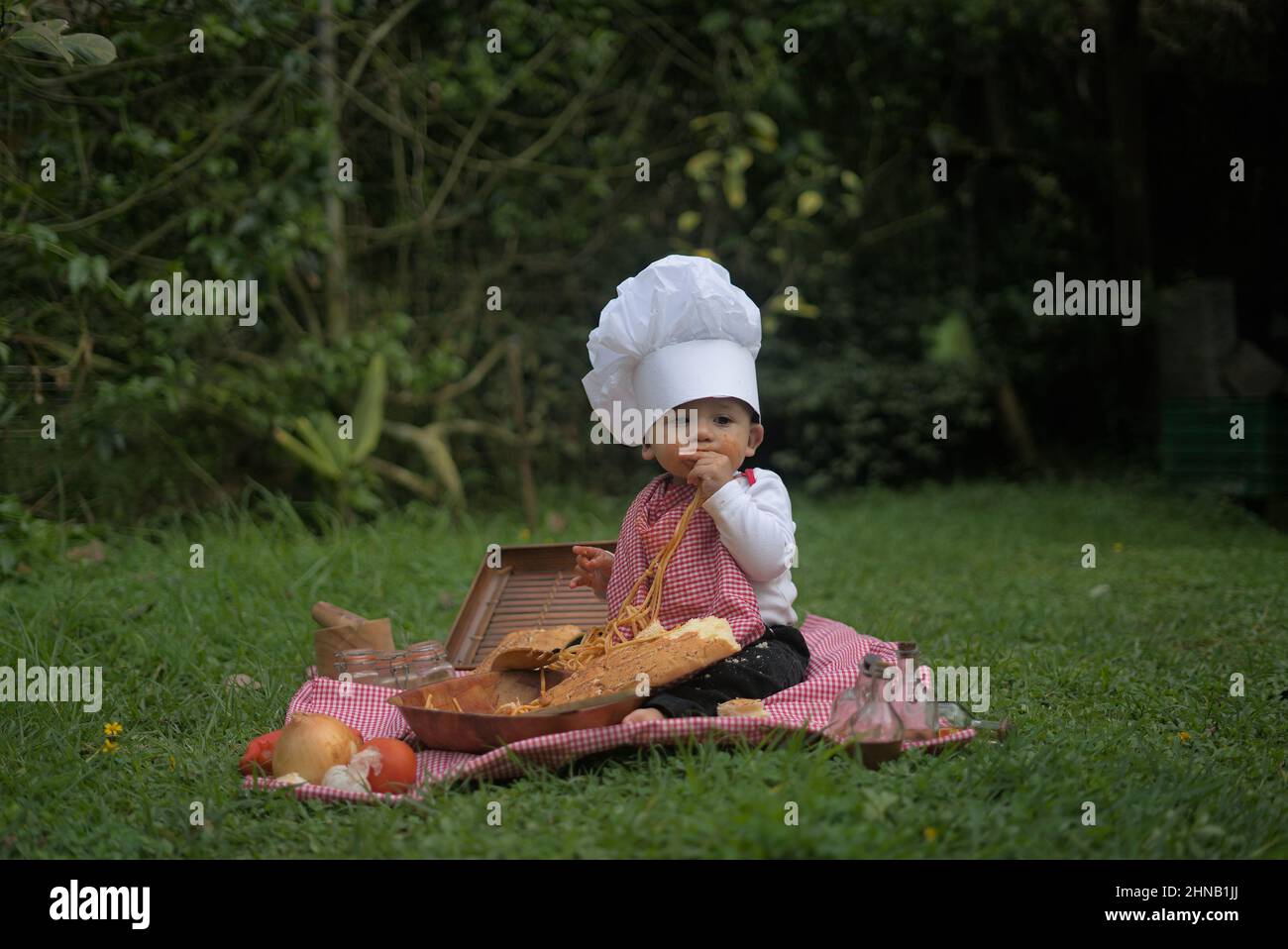 Adorable Caucasian child doing a picnic on the grass in a chef uniform Stock Photo