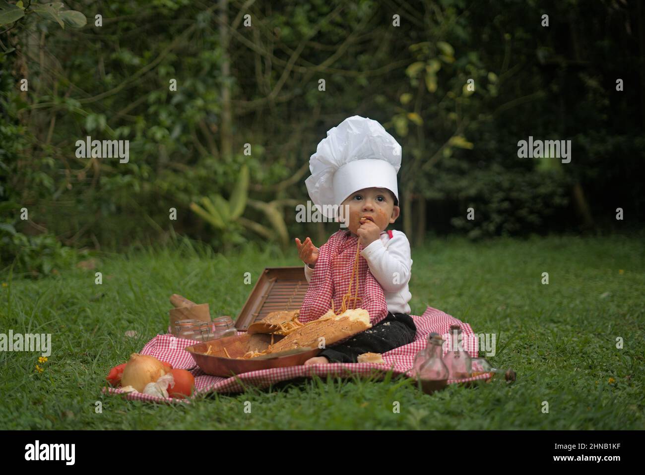 Adorable Caucasian child doing a picnic with pasta on the grass in a chef uniform Stock Photo