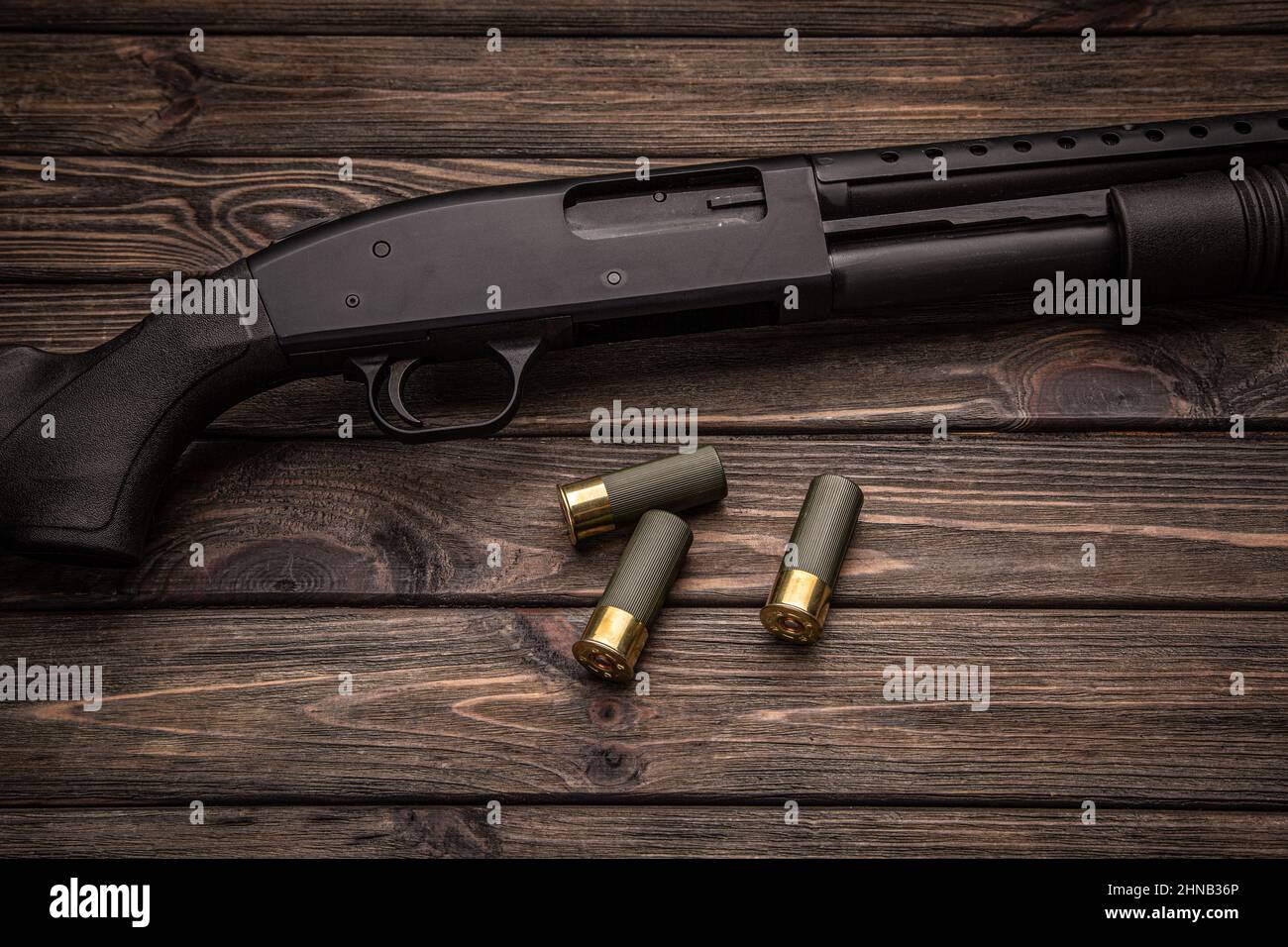 A black 12-gauge pump-action shotgun and ammo are on a wooden table. A  smooth-bore weapon with a plastic stock. Dark brown background Stock Photo  - Alamy