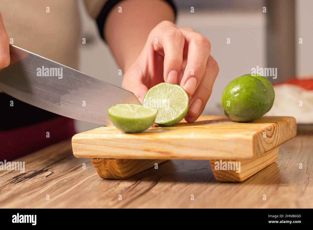 person cutting a green lemon with a knife on wooden table in his kitchen Stock Photo