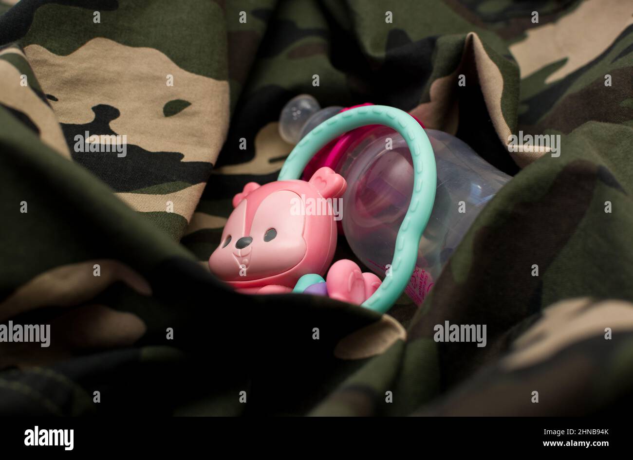 Rattle toy and baby bottle on military uniform, close up. Love and war concept Stock Photo