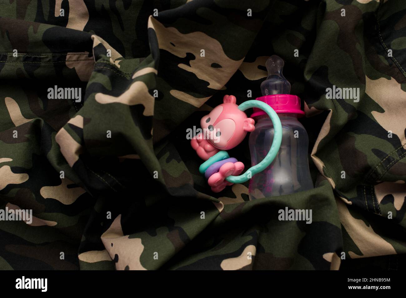 Rattle toy and baby bottle on military uniform, top view. Love and war concept Stock Photo