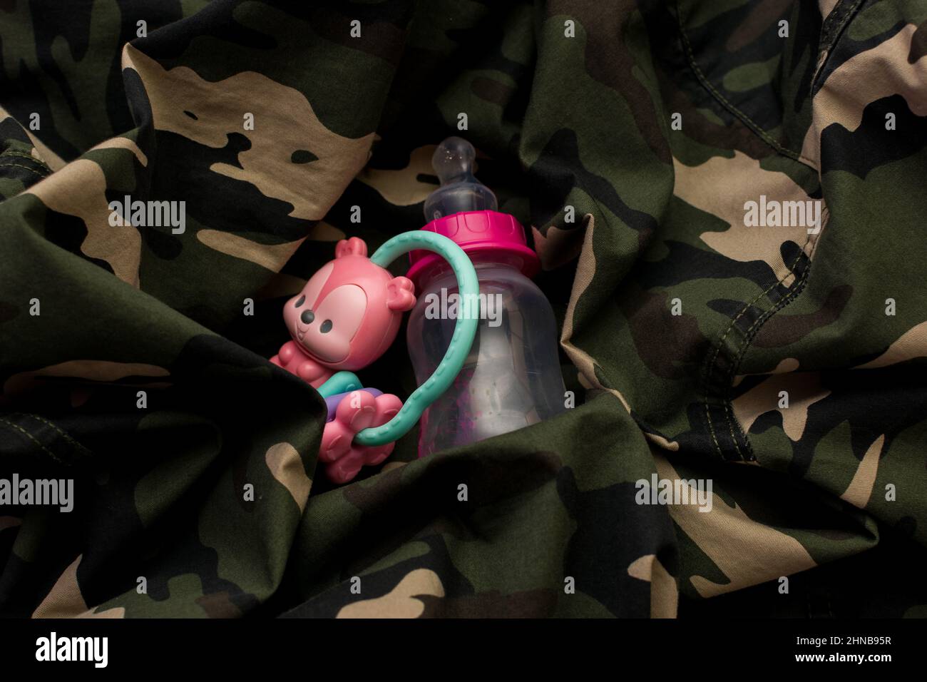 Rattle toy and baby bottle on military uniform. Love and war concept Stock Photo