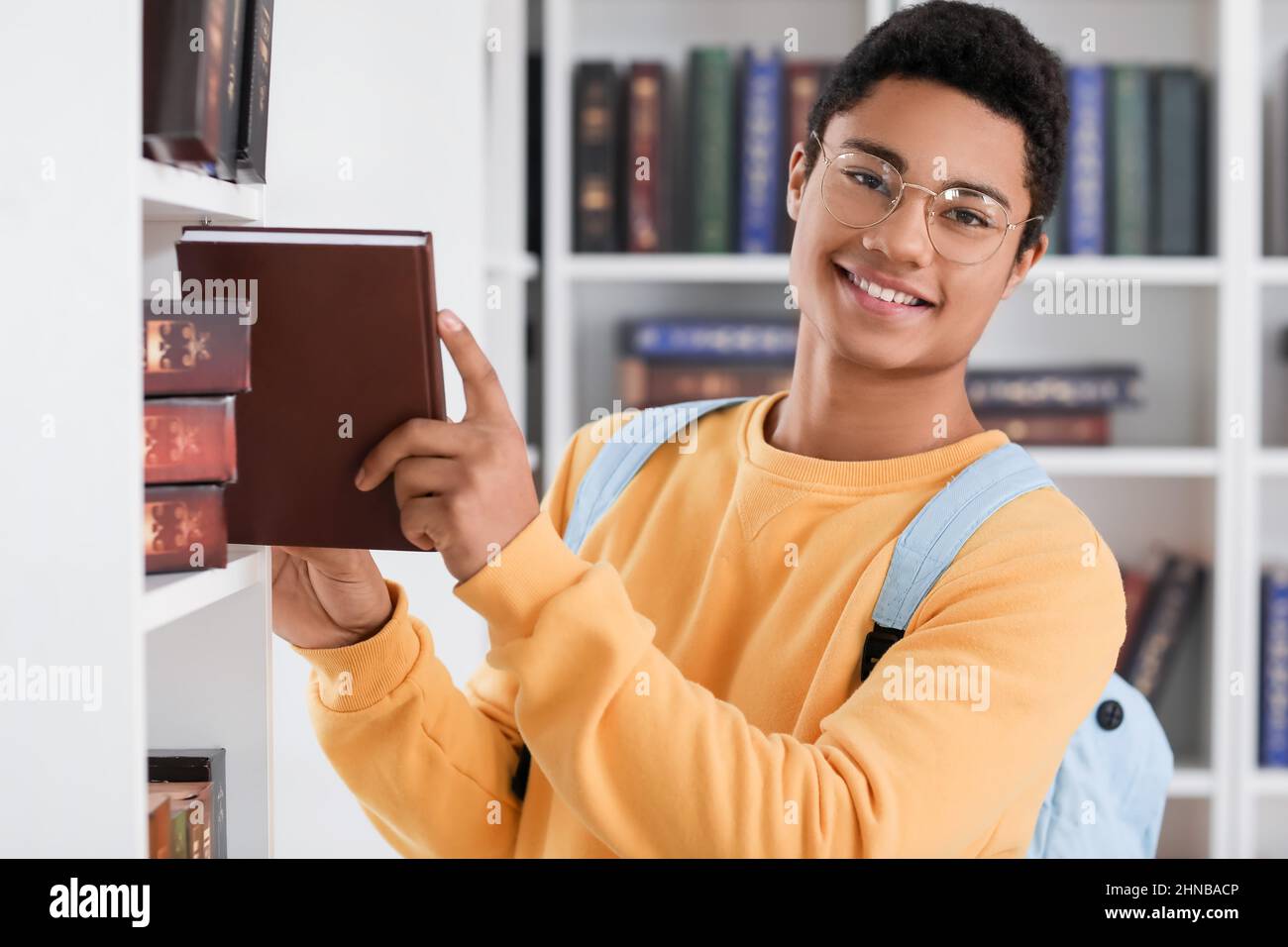 Male AfricanAmerican student taking book from bookshelf in library