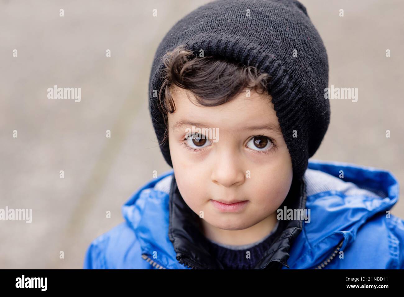 Little boy looking at you, staring wearing a blue rain jacket and black