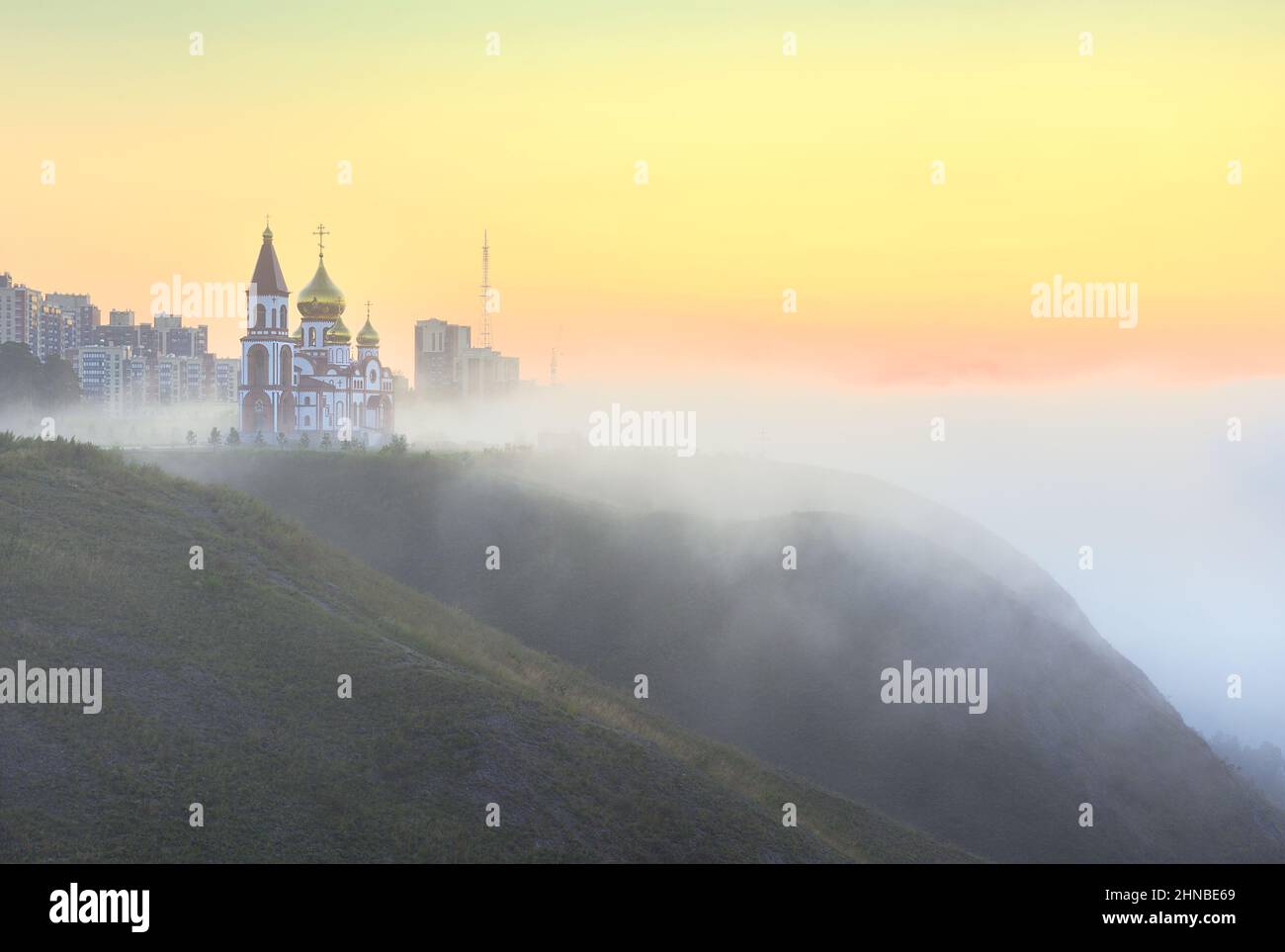 Orthodox Church in the morning fog on a steep coastal cliff. Krasnoyarsk, Siberia, Russia Stock Photo