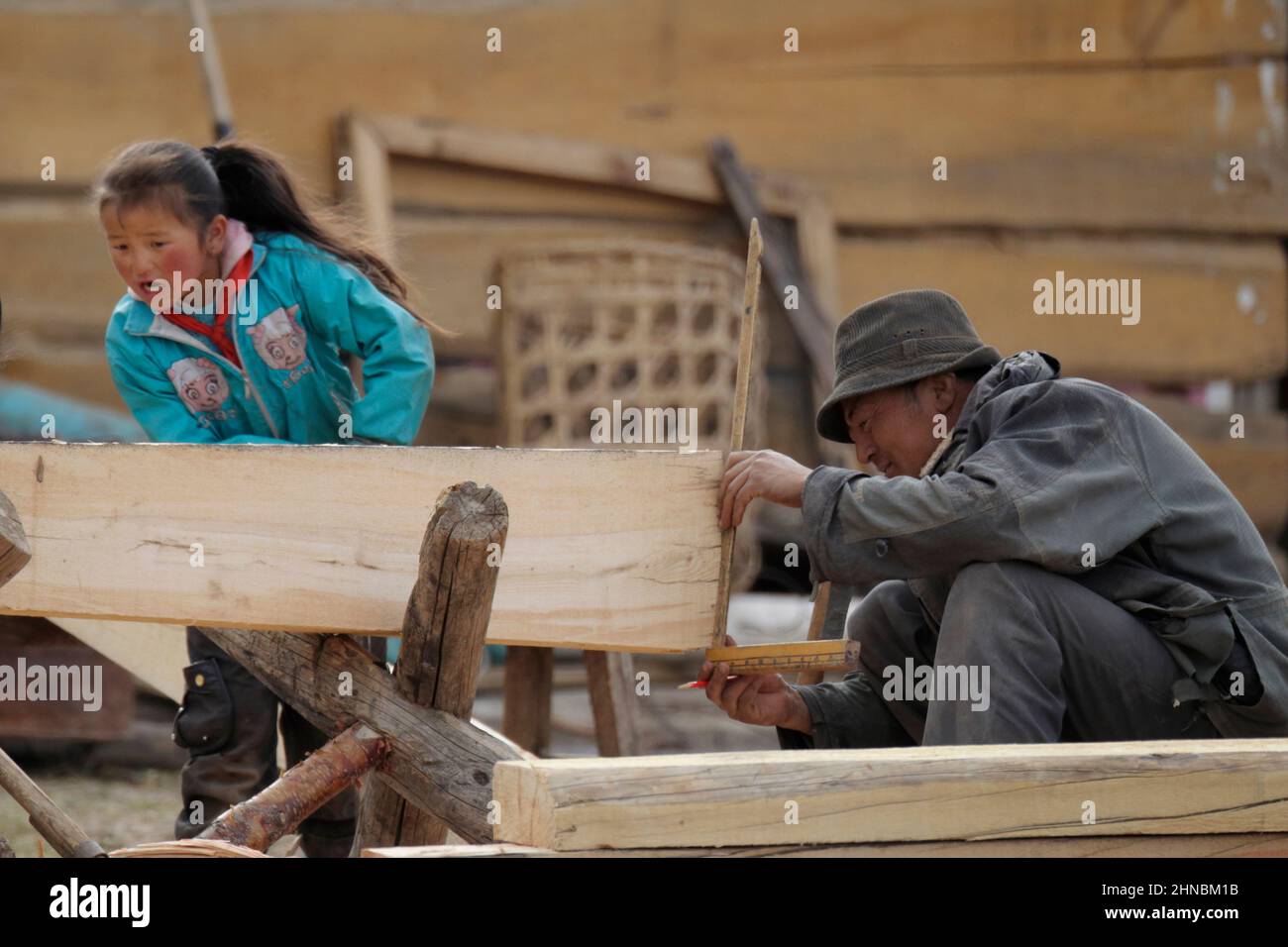 Chinese carpenter measuring a plank of wood with daughter "helping