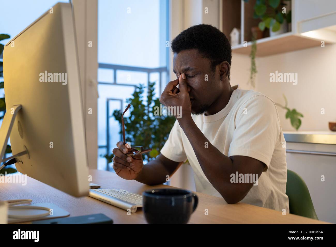 Tired guy remote web developer take off glasses feel eye strain after overtime computer work at home Stock Photo