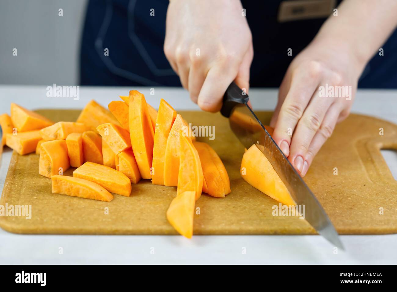 woman cutting with knife sweet potato into wedges on wooden board. Stock Photo