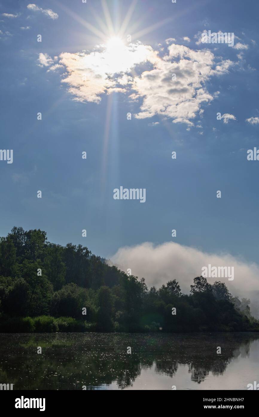 sun rays breaking through clouds floating above surface of water Stock Photo