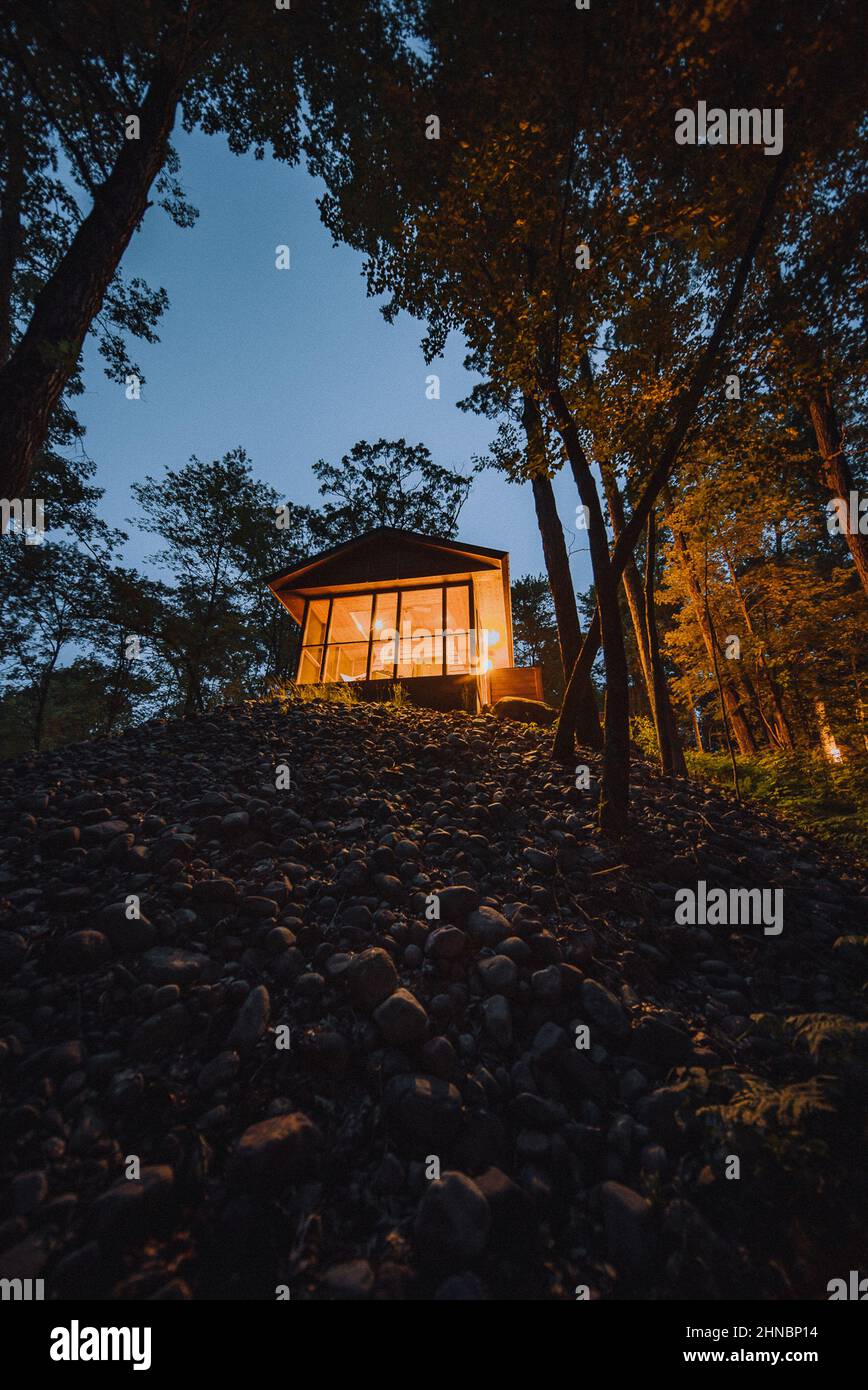 Vertical shot of a amall cabin in the woods on top of a hill surrounded ...