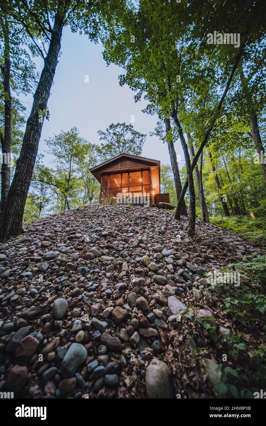 Vertical shot of a amall cabin in the woods on top of a hill surrounded ...