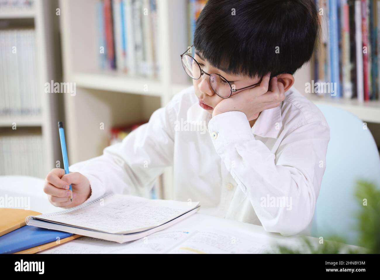 A child who is tired of boring school homework and studying is studying hard by taking notes in a notebook even though he is tired. Stock Photo