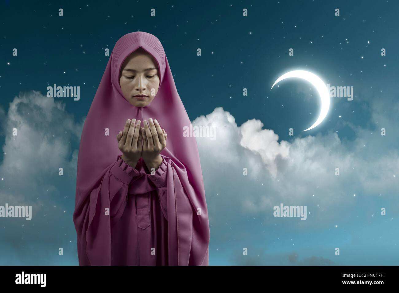 Asian Muslim woman in a veil standing while raised hands and praying ...