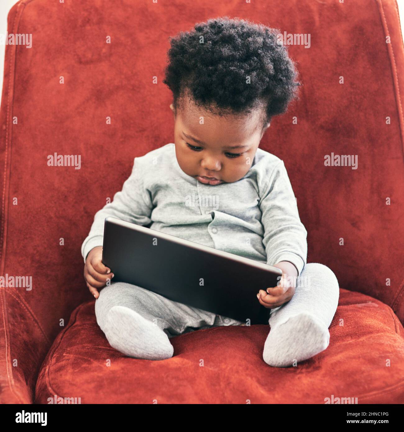 I need to check my emails.... Shot of a little baby boy sitting in a chair holding a digital tablet. Stock Photo