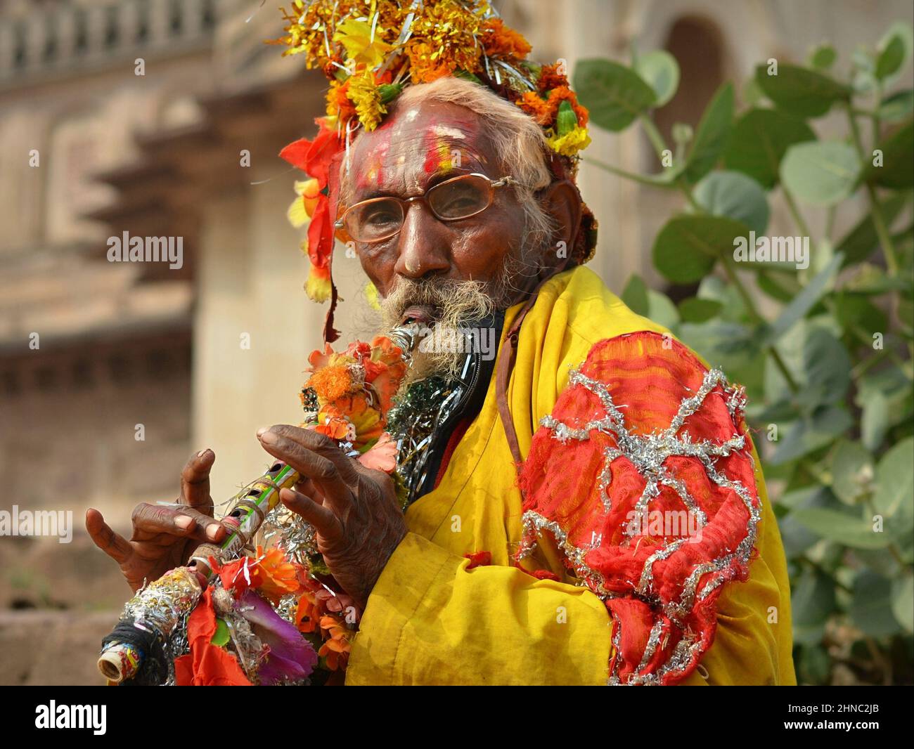 Old Indian temple musician with bansuri flute wears colorful motley outfit, plays his instrument at Lakshmi Narayan Mandir temple and looks at viewer. Stock Photo