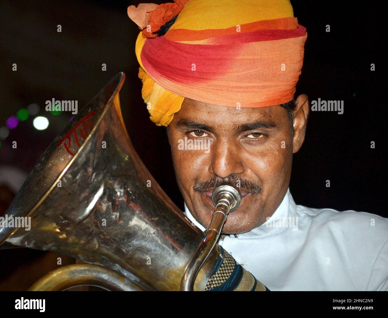 Young turbaned euphoniumist from a marching Indian British brass band plays at night his traditional euphonium instrument and looks at the camera. Stock Photo