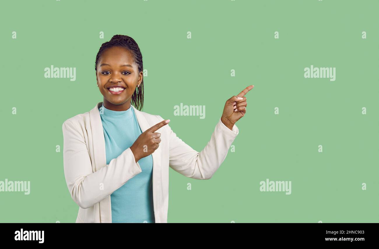 Happy young black businesswoman smiling and pointing at green copy space background Stock Photo