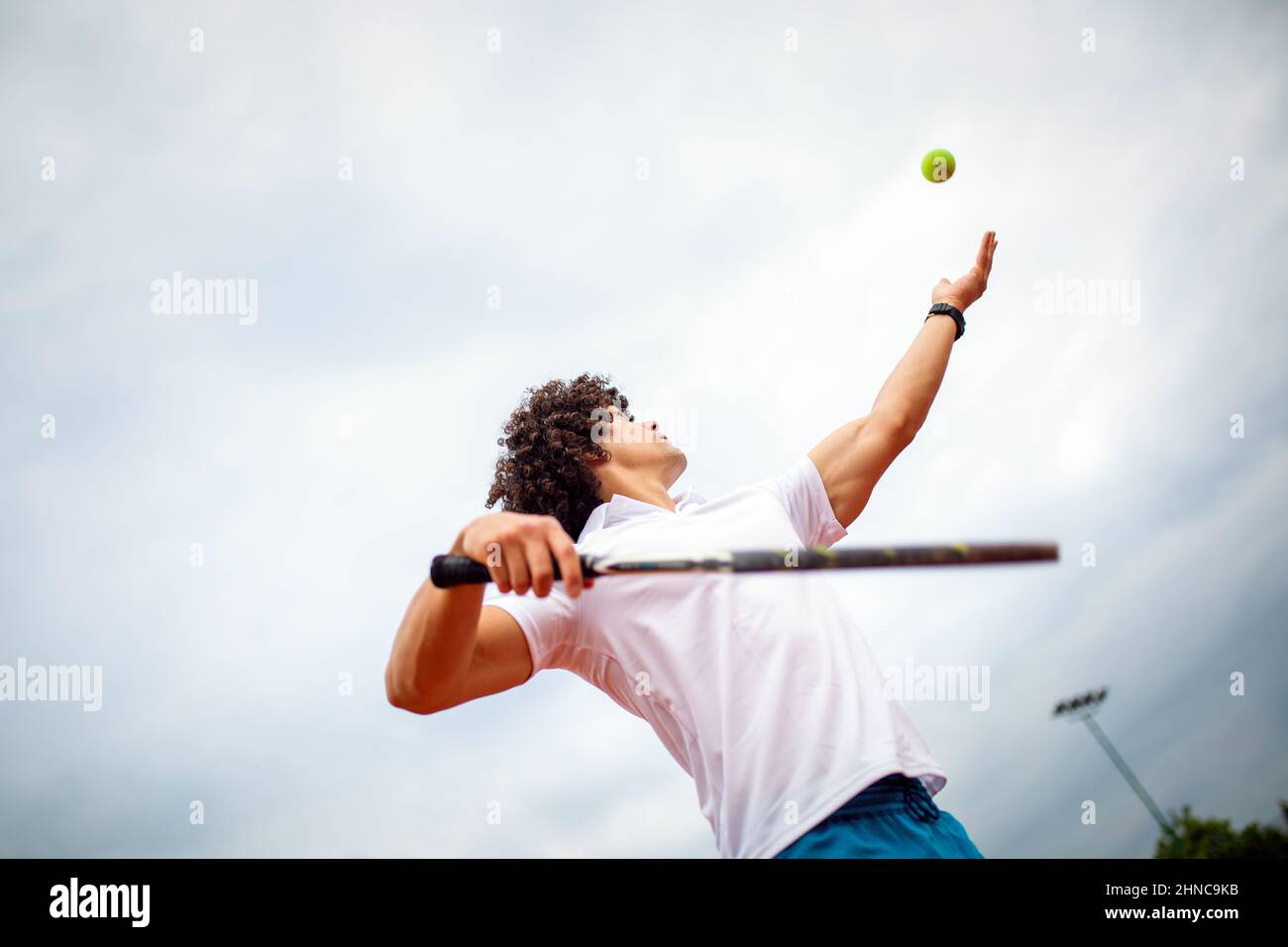 Young handsome tennis player with racket and ball prepares to serve at beginning of game or match. Stock Photo