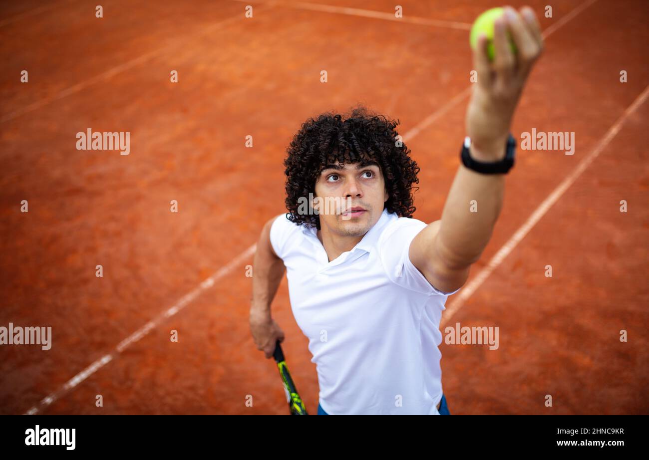 Young handsome tennis player with racket and ball prepares to serve at beginning of game or match. Stock Photo