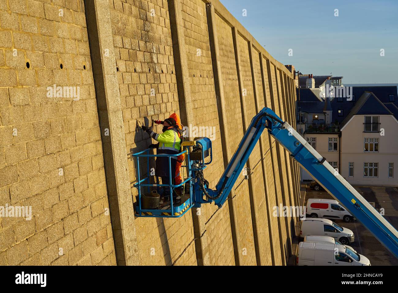 Men repair a high cliff wall on a boom arm Stock Photo