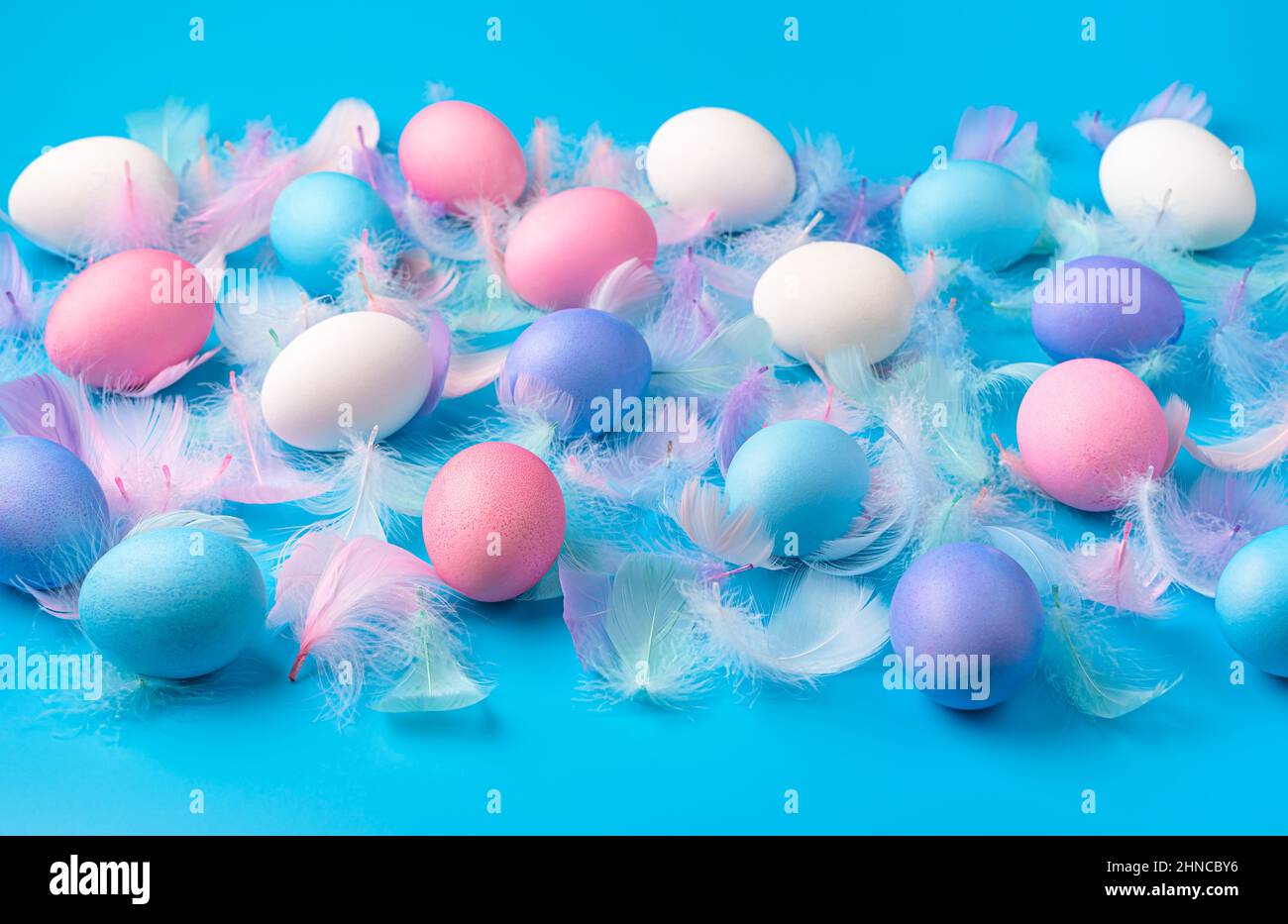 Easter background with colored eggs and feathers on a blue background. Side view. Stock Photo