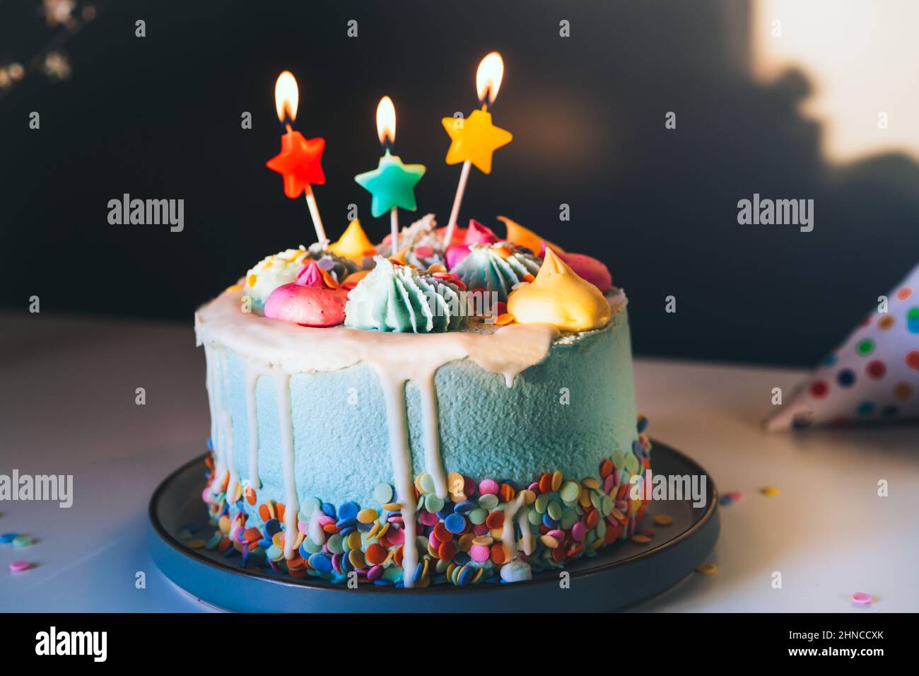 Colorful birthday cake with sprinkles and burning star shaped candles ...