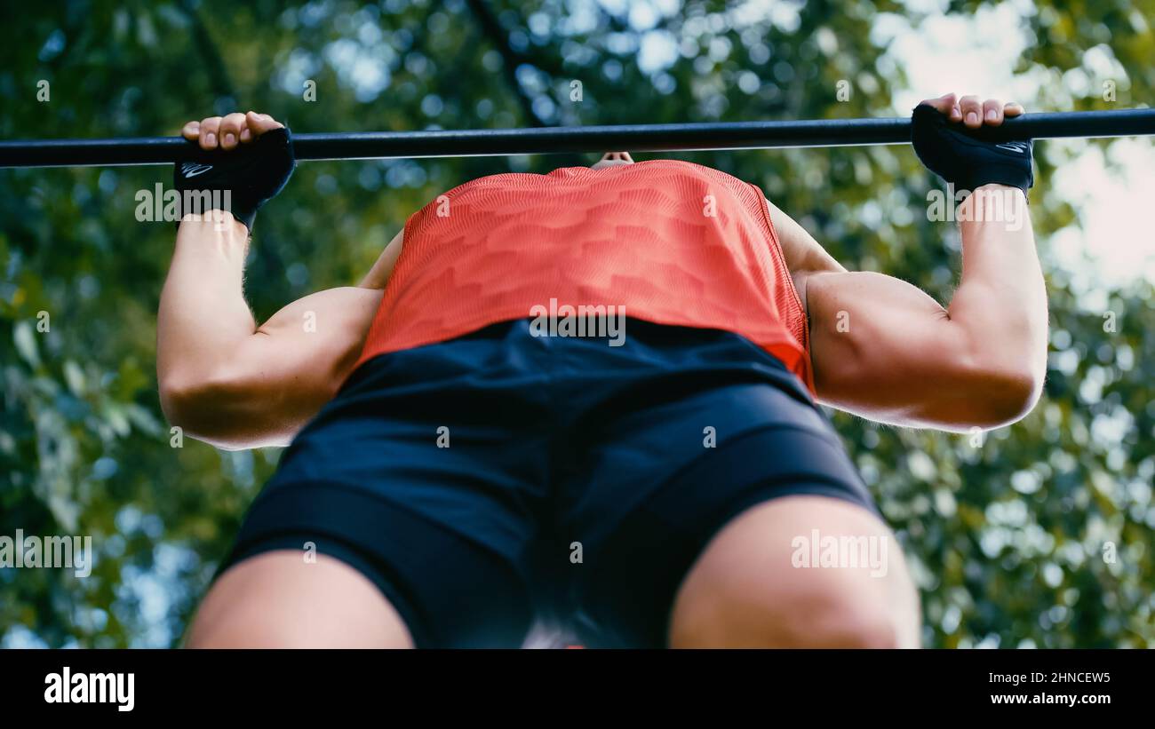 bottom view of young sportsman doing pull ups on horizontal bar outside ...