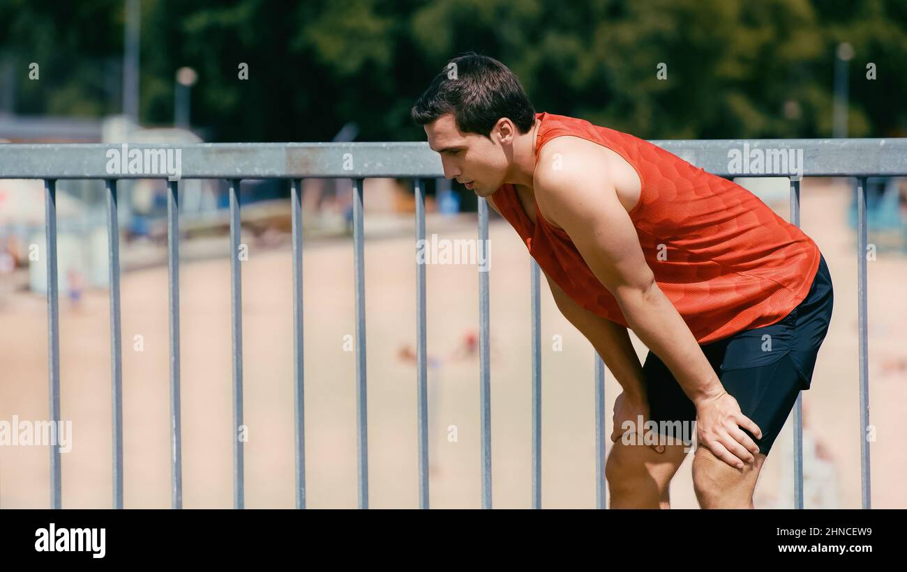 young sportsman breathing while resting after jogging on bridge Stock
