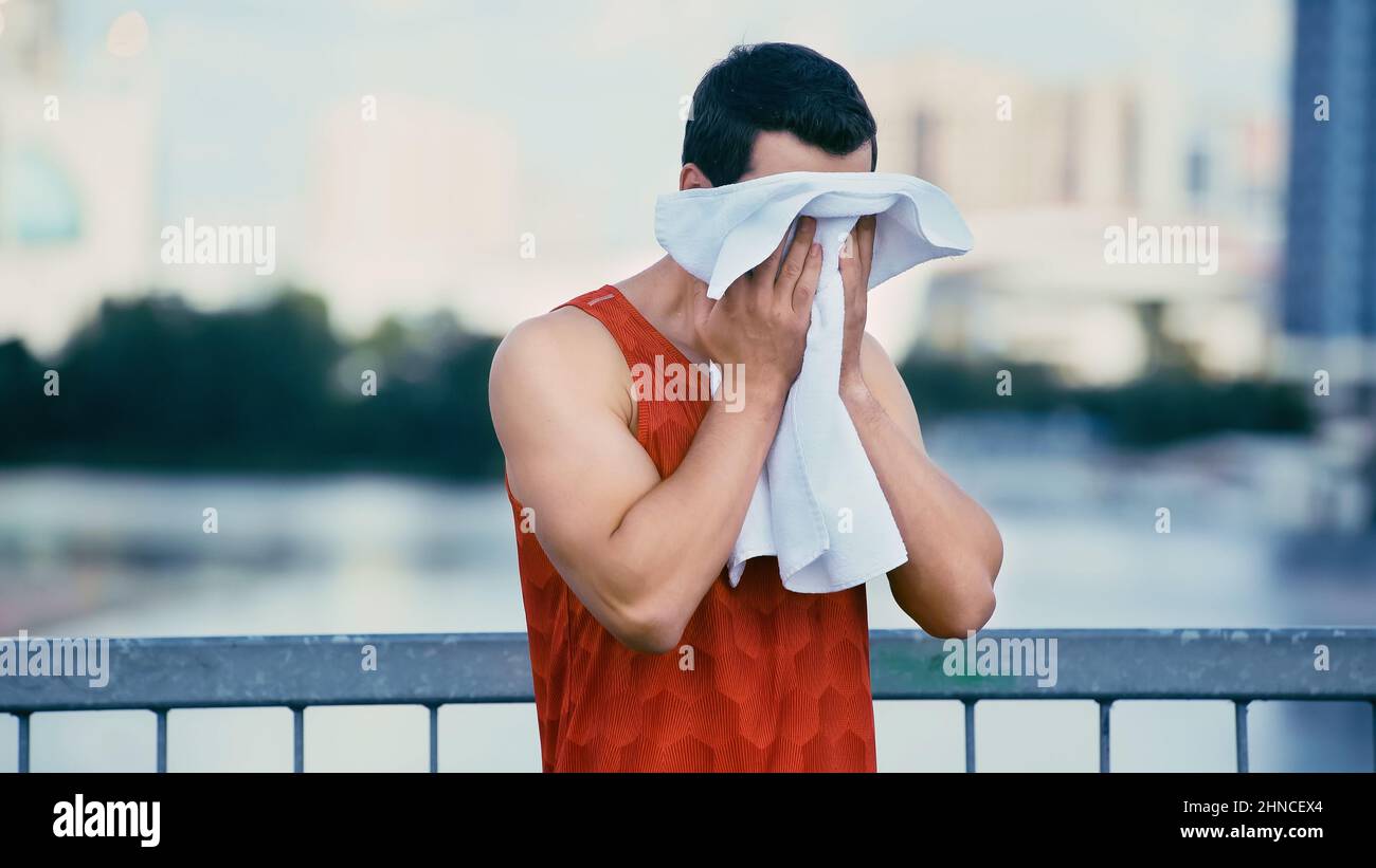 young sportsman wiping face with towel while standing on bridge Stock