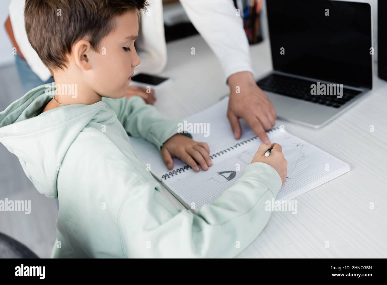 Preteen boy writing on notebook near father and laptop at home Stock Photo