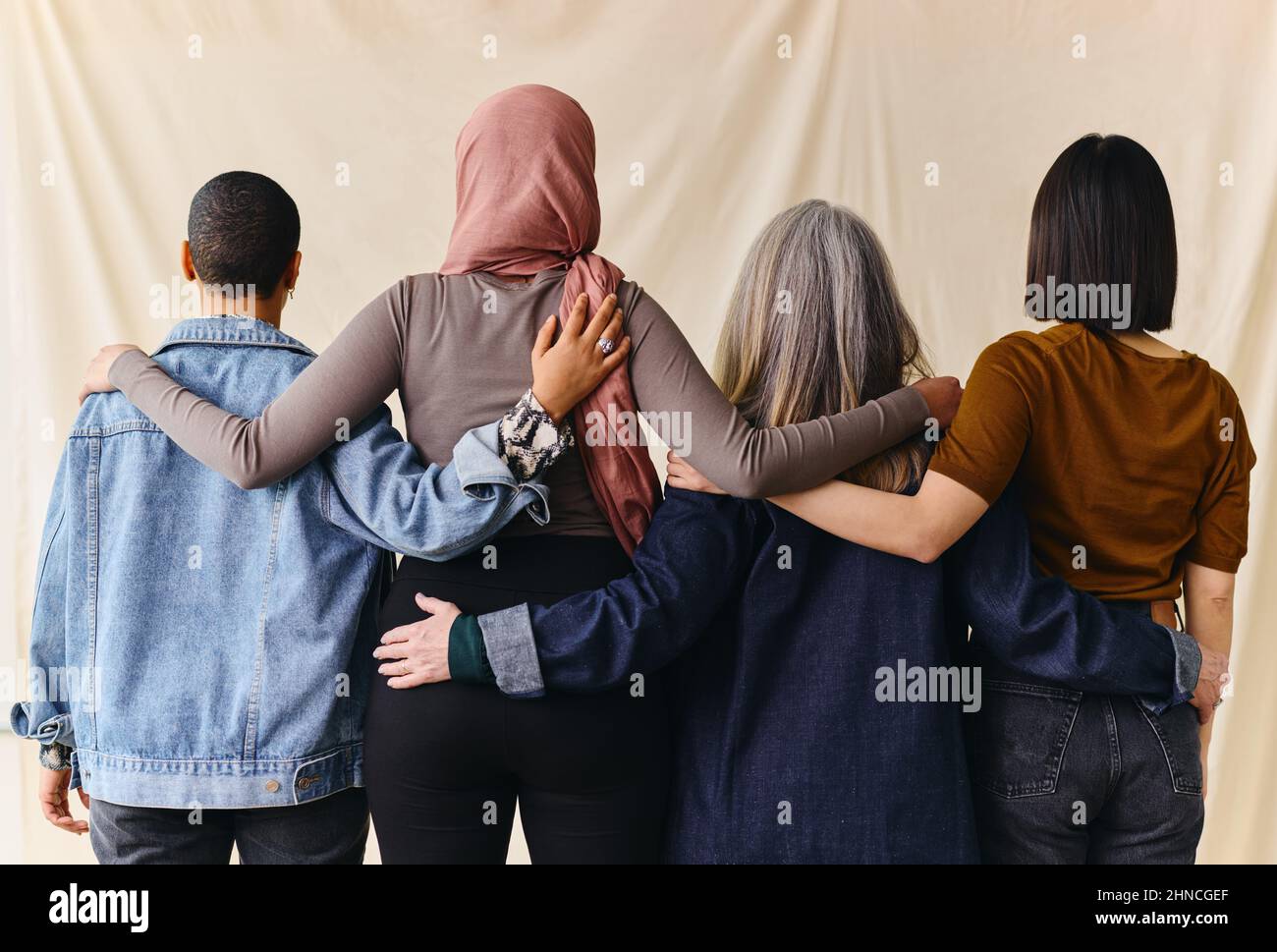Rear view of four women with arms around each other in support of International Women's Day Stock Photo