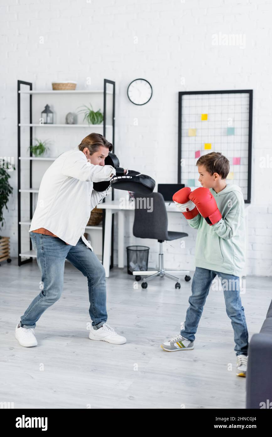 Kid in boxing gloves training with dad in punching pads at home Stock Photo 