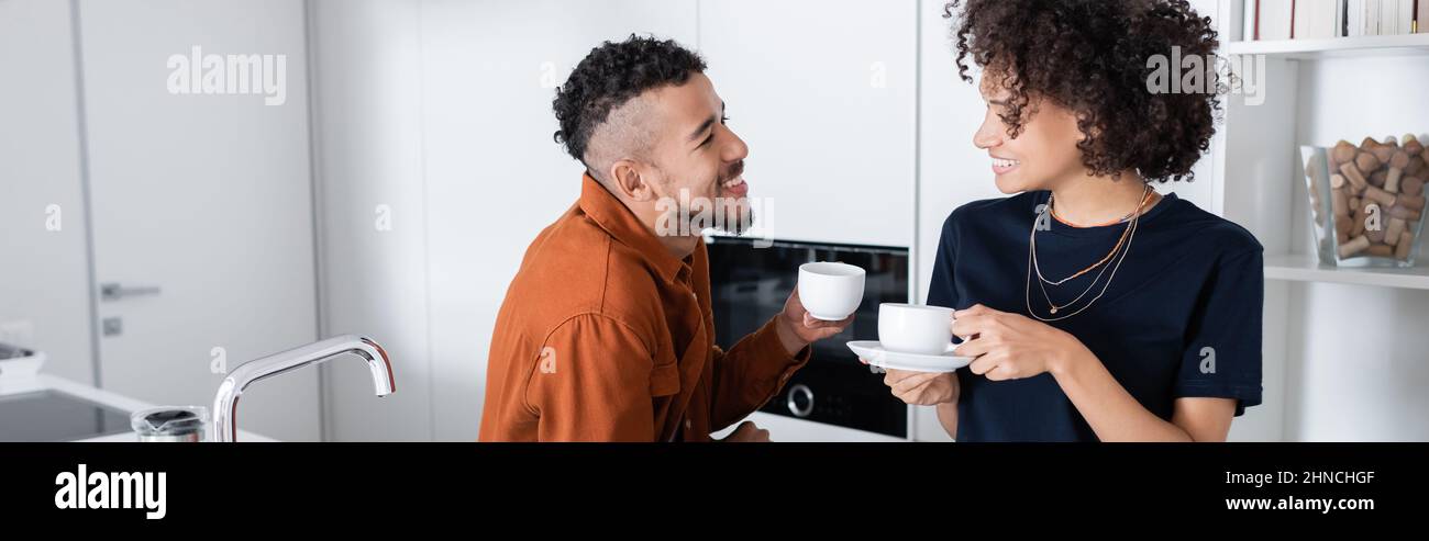 happy african american couple holding cups of coffee in kitchen, banner ...